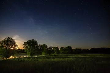 Foto op Canvas Sterren van de Melkweg aan de nachtelijke hemel. Een zicht op de sterrenhemel achtergrondzonsondergang verlichtte de horizon. © olgapkurguzova