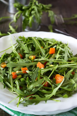 Salad of fresh arugula in a plate on a dark wooden background
