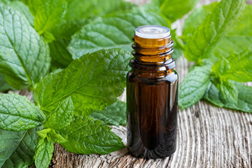 A bottle of peppermint essential oil with fresh peppermint leaves