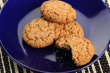 A bitten cookie on a plate. A lot of oatmeal cookies on a blue plate. View from above.