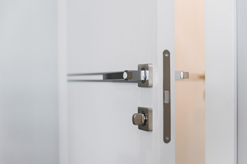 Modern chrome door handle and lock on white wooden door. Close-up elements of the modern interior of the apartment. Ajar white door.