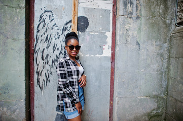 Obraz na płótnie Canvas Hip hop african american girl on sunglasses and jeans shorts. Casual street fashion portrait of black woman.