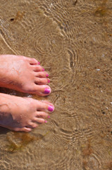 Female feet in the sand sea. Feet in water.