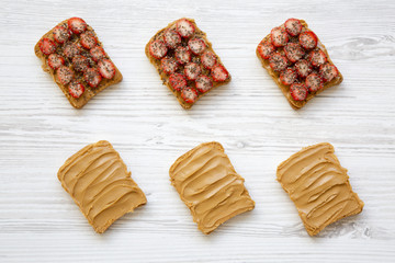 Top view, toasts with peanut butter, strawberries and chia seeds on white wooden surface. Healthy dieting. Close-up.