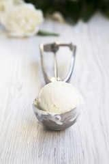 Vanilla ice cream in ice cream scoop on white wooden background, side view.