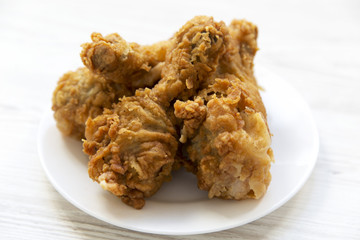 Fried chicken drumsticks on a white plate, side view.