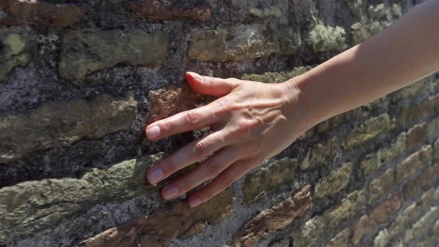 Woman drawing hand against old ancient red brick wall in slow motion. Female hand touching hard rough surface of stone bridge