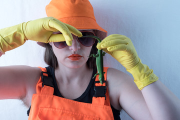 Slender girl in orange fashionable semi-overalls, orange hat and yellow household gloves, with...