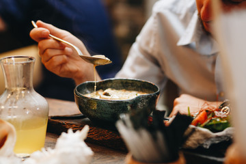 a man eats freshly cooked creamy mushroom soup in a dark clay dish.