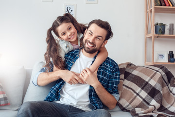Father and little daughter at home sitting hugging looking camera joyful