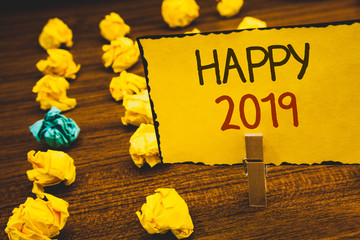 Fototapeta premium Handwriting text Happy 2019. Concept meaning New Year Celebration Cheers Congrats Motivational MessageClothespin holding Yellow paper ideas crumpled papers wooden background.