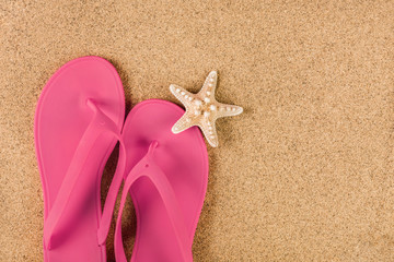 Pink sandal flip flop on sand beach and starfish. Summer vacations copy space and concept. Top view, close up