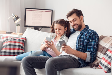 Father and little daughter at home sitting hugging browsing smartphone joyful