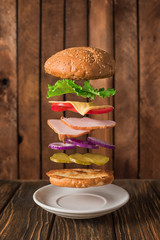 Fresh sandwich with flying ingredients isolated on wooden background