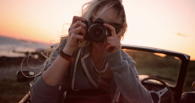 Woman on road trip sitting in convertible and taking photos