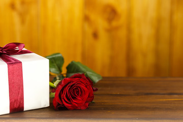 Red roses and gift box on brown wooden table