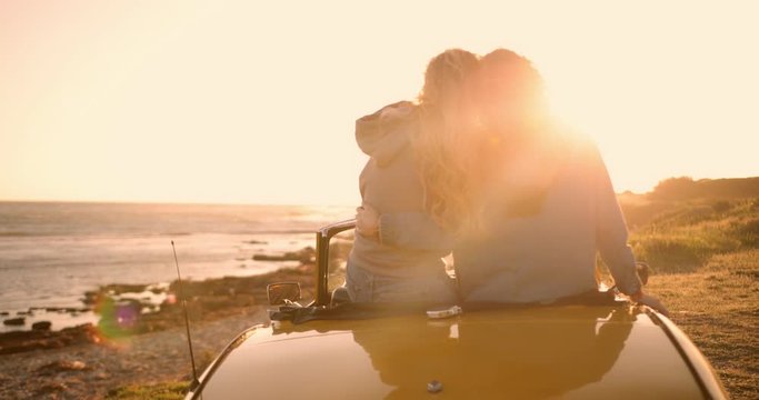 Young women with convertible car relaxing at beach at sunset