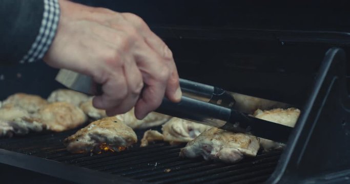 Hand of senior man turning chicken on barbecue