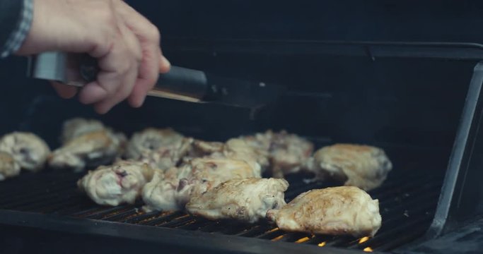 Hand of senior man moving chicken pieces on barbecue