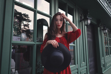 Elegant brunette young woman wearing red dress and straw hat on the street cafe. Fashion and style.