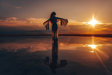 Elegant woman dancing on water. Sunset and silhouette