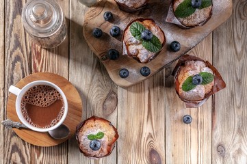 Muffins with blueberries and a cup of hot chocolate on a wooden background. homemade baking. Top view