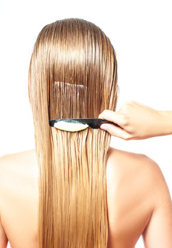 Woman with comb is applying hair conditioner on her wet blonde hair