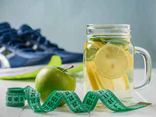 A freshly prepared drink made of lemon and mint and apple on a white table and sneakers.