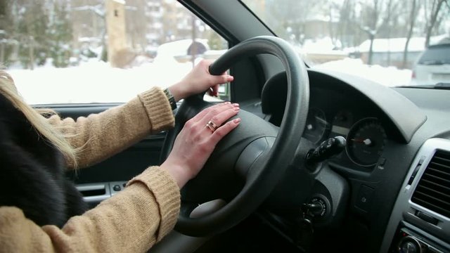 Close-up of female hands on steering wheel while driving a car in winter. The girl with the manicure keeps hands on the steering wheel of the car.
