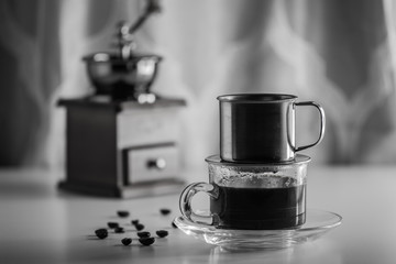 Coffee beans on white wooden with black coffee in clear glass and Coffee grinder on background.