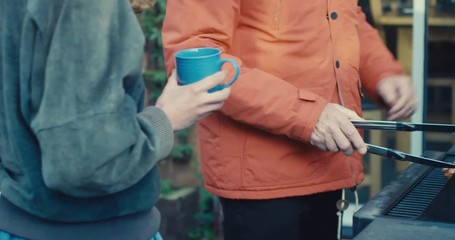 Senior man doing barbecue whilst talking to young woman