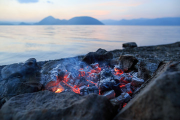 Glowing ashes smoldering in a stone fire ring on the shore of Lake Koya in Hokkaido, Japan