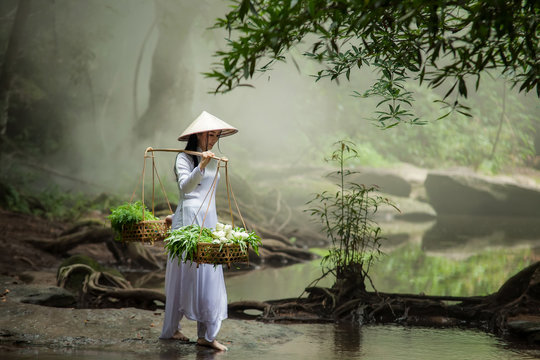 Beautiful woman wearing a hat Dress Ao Dai traditional Vietnamese dress standing in the forest.