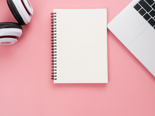 Blank notebook, headphone and laptop on pink background.
