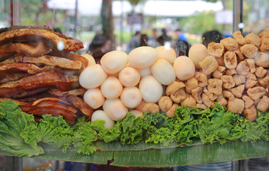 Fried pork with egg and tofu in glass cabinet for Chinese roll noodle soup.