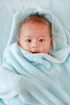 Portrait of cute infant baby boy in towel lying on bed after bath.