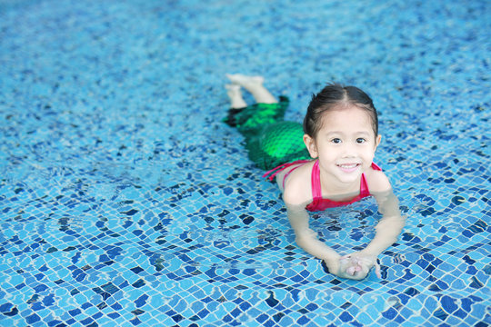 Portrait of cute little Asian child girl wear mermaid swimming suit has fun at the pool.
