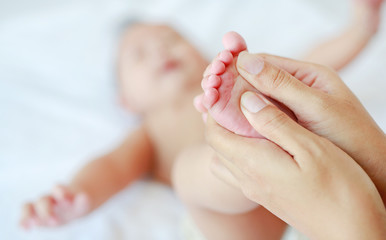 Mother hand massaging feet of infant baby on the bed at home.