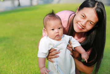 Asian mother holding her son to relax in the green grass garden with morning sunrise.