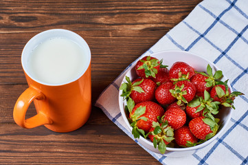 strawberry in a white bowl on napkin with mug of milk cream on wooden background