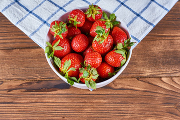 strawberry in a white bowl on cage napkin on a wooden background