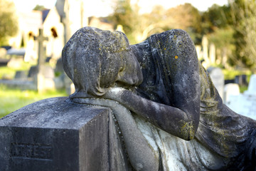 Old stone statue of woman feeling pain the loss of a loved in an old English cemetery.