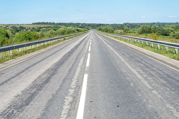 Vanishing straight highway with metal rails along. Kozelsk, Kaluzhsky region, Russia.