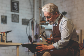 An elderly shoemaker in a workshop - 210270513