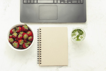 Workplace. Laptop, notebook, in a white bowl of strawberries and a refreshing drink with ice and mint. Top View, flat lay.