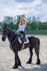Fototapeta na wymiar Woman enjoying horse company. Young Beautiful Woman in straw hat With black Horse Outdoors, stylish girl at american country style 