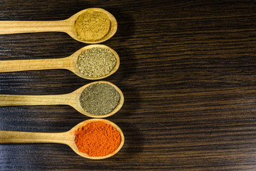 Spoons with the different spices on dark wooden table. Top view