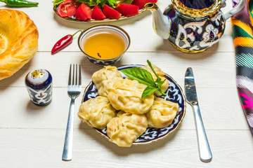 traditional Uzbek dish Manta with potatoes, meat and pumpkin, Uzbek ж, tomatoes and cucumbers on plates with national ornaments on a white wooden background