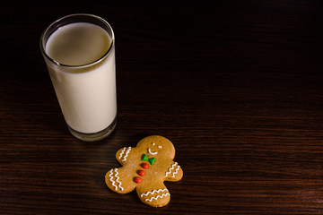 Gingerbread man and a glass of milk on a dark wooden table