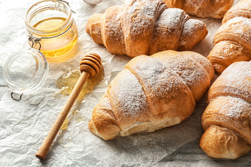 Tasty croissants and honey on parchment paper